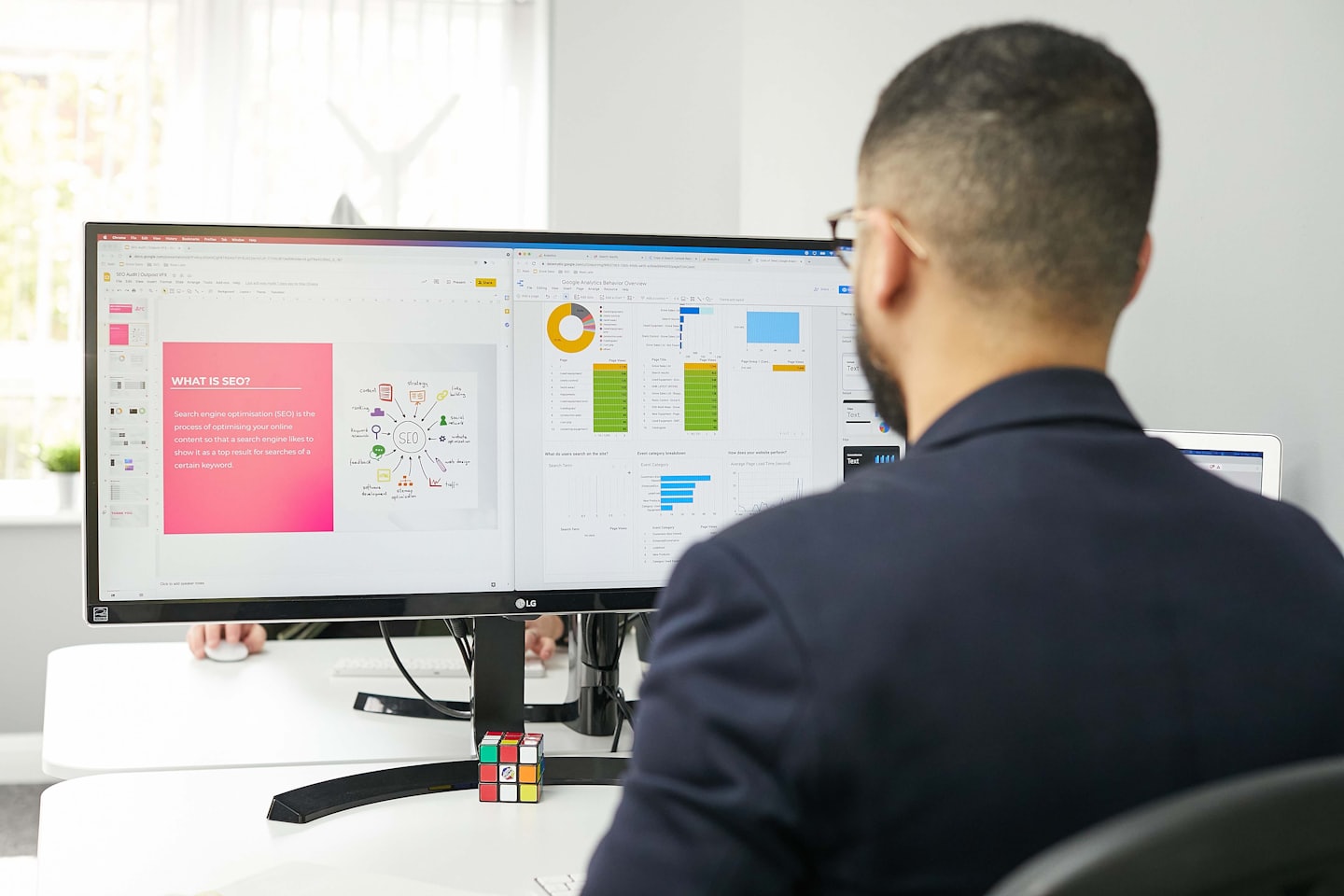 Man works on dual computer monitors displaying SEO and analytics.