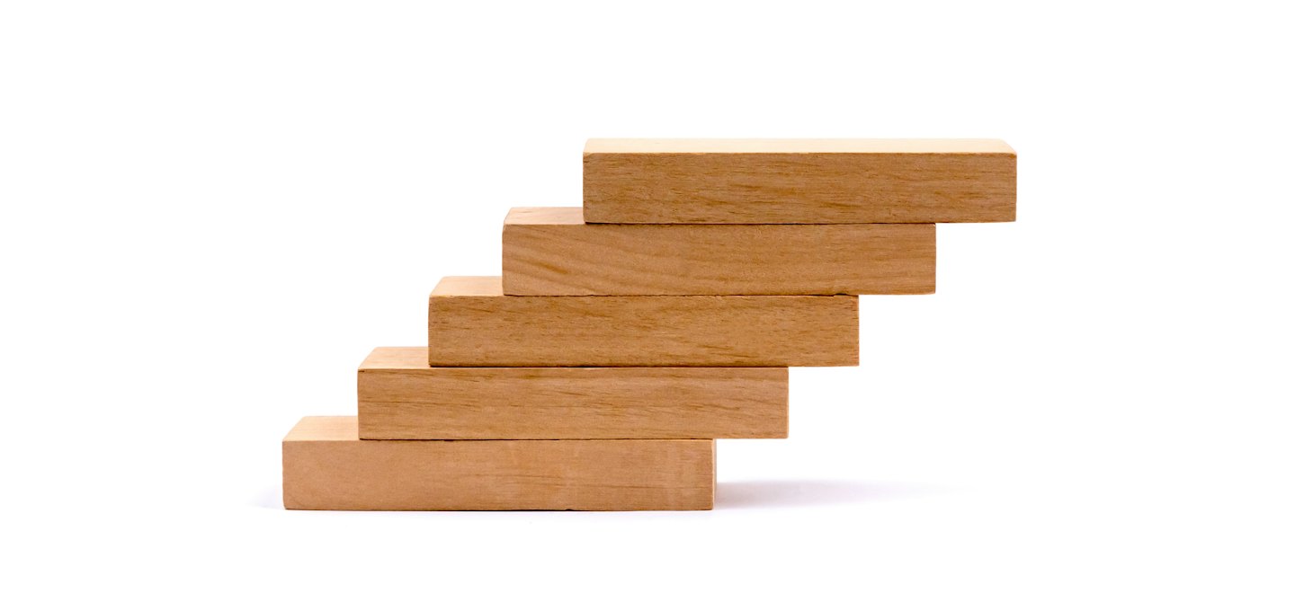 Five light brown wooden blocks stacked in ascending staircase formation.