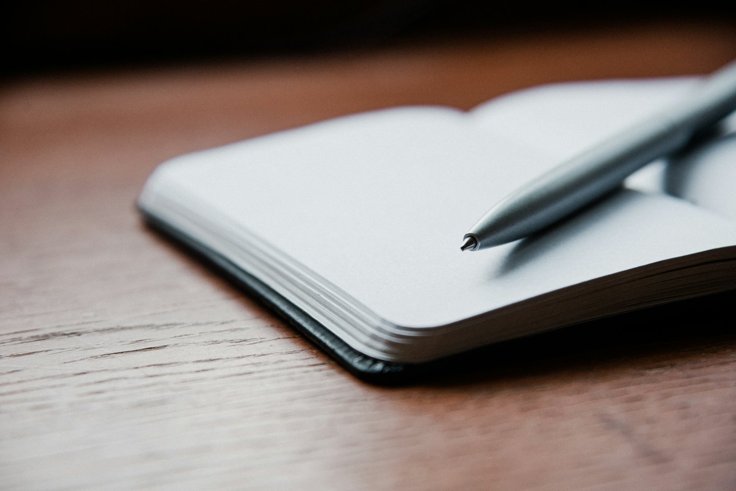 White notebook and silver pen on a wooden desk.