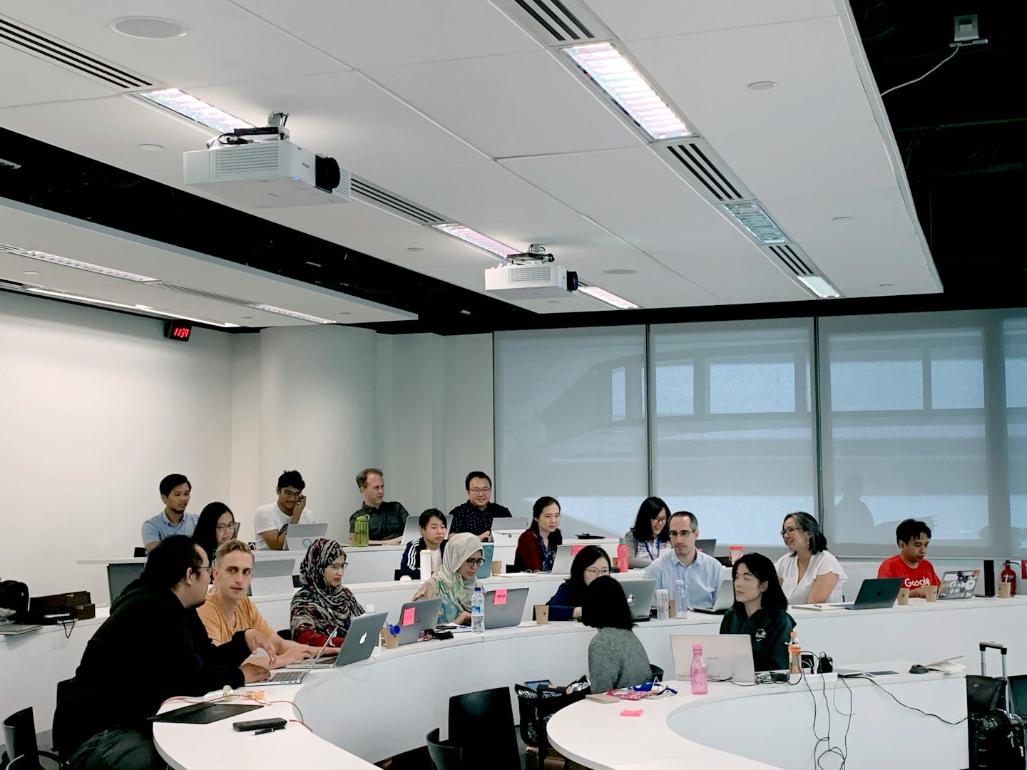 Diverse adults collaborate and learn on laptops in a modern classroom.